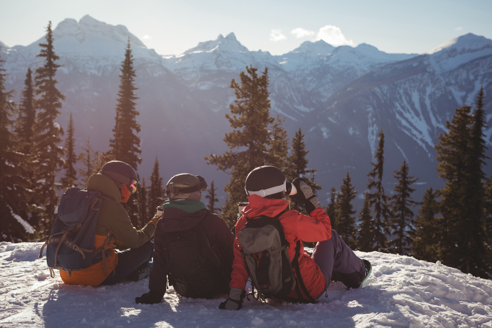 three skiers having coffee on top of a snowy mountain