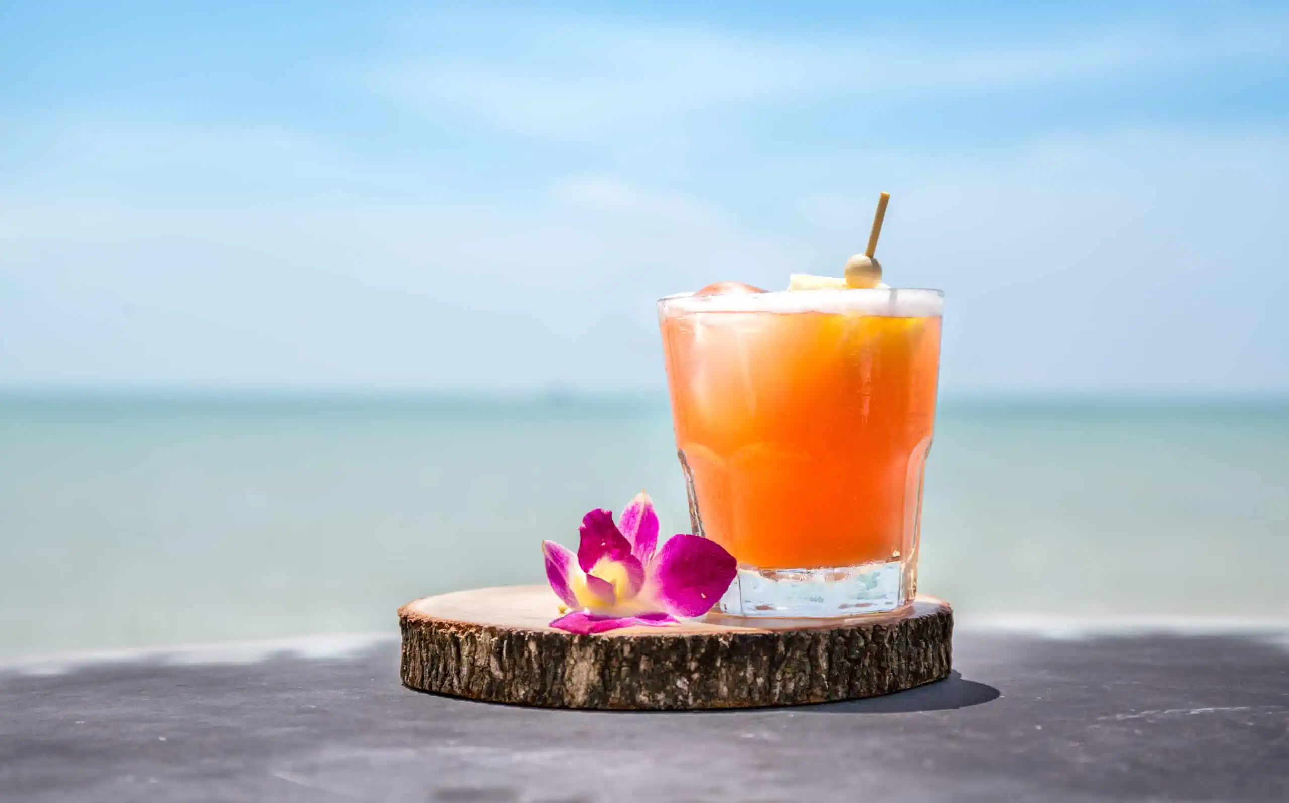 orange cocktail drink beside a pink flower